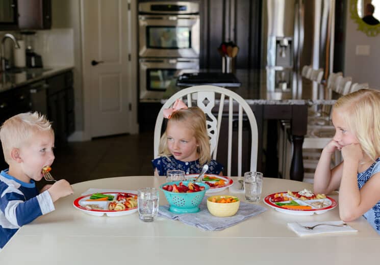 3 kids sitting at a dinner table eating and learning table manners