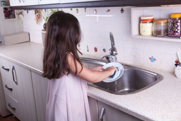 little girl cleaning a dish in the kitchen