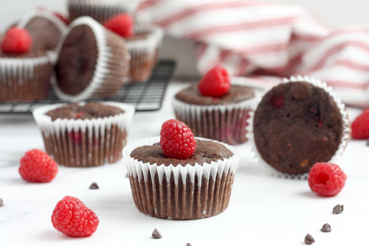 chocolate raspberry bran muffins scattered on the counter with raspberries and chocolate chips