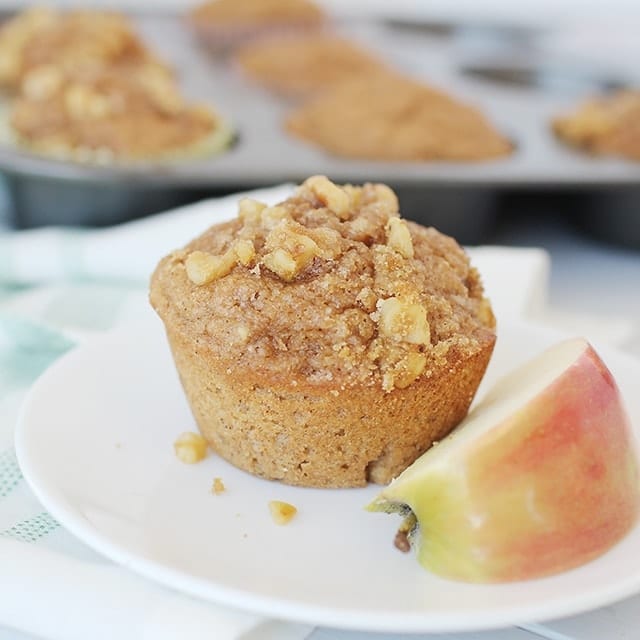 Applesauce muffins with nuts and brown sugar on a plate with a slice of apple