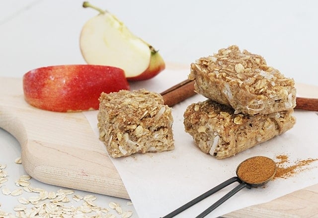 apple cinnamon breakfast bars on a wooden cutting board with sliced apples and cinnamon sticks in the background