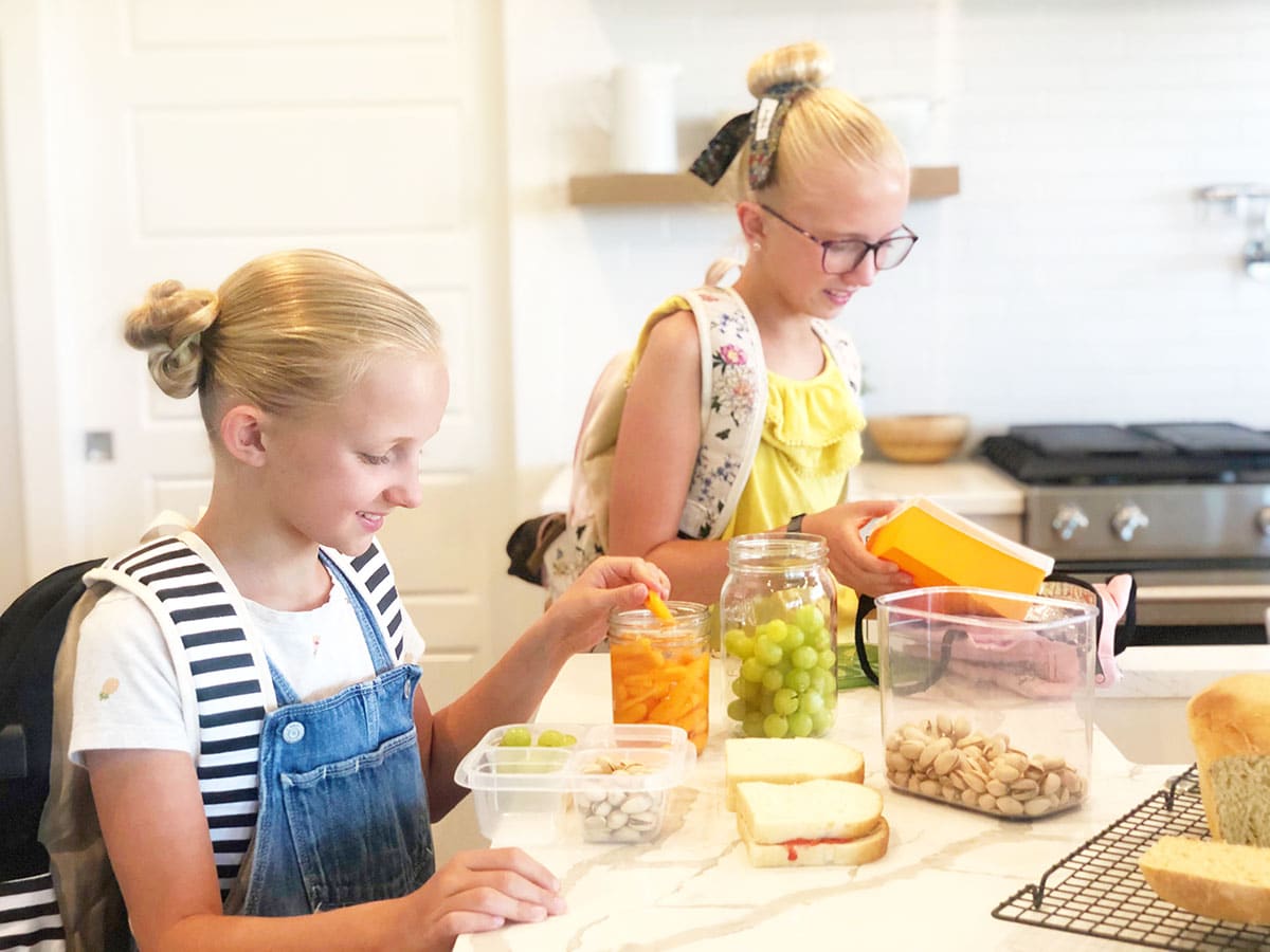 two girls with backpacks packing their lunches for school in the morning