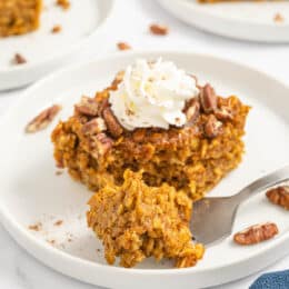 a square of baked pumpkin oatmeal on a white plate with a piece taken out with a fork