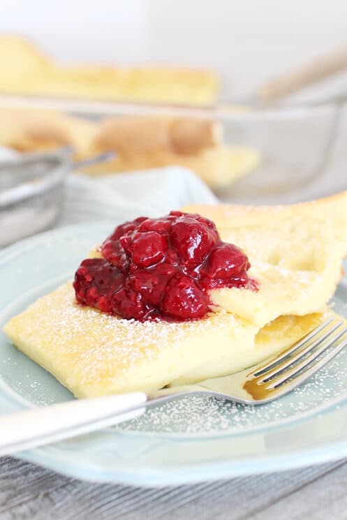 German pancakes with raspberry jam and powdered sugar served on a blue plate