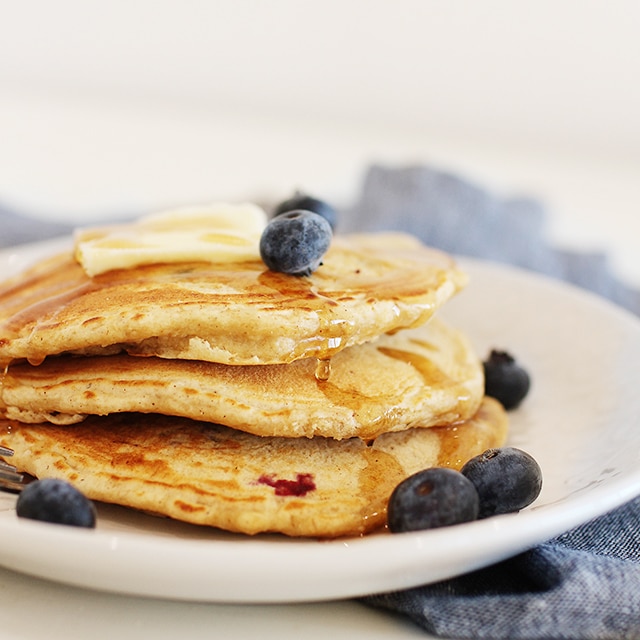 pancakes topped with butter, blueberries, and syrup on a white plate with a blue napkin