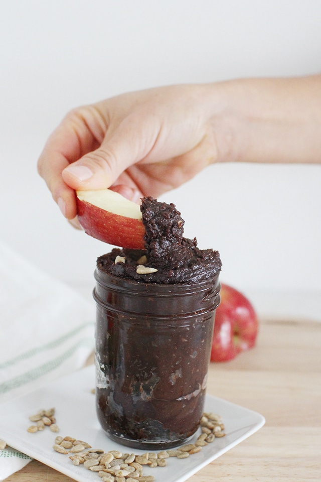 dipping apple slice in a jar of homemade chocolate sunbutter