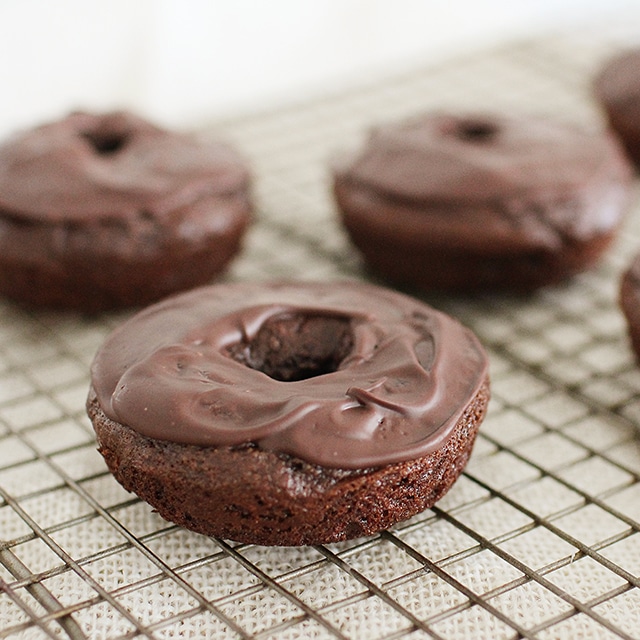Make rich, chocolatey, homemade donuts right in your own kitchen! These donuts are baked, not fried, and even include a surprise ingredient that makes them a more balanced treat. homemade chocolate donuts on cooling rack