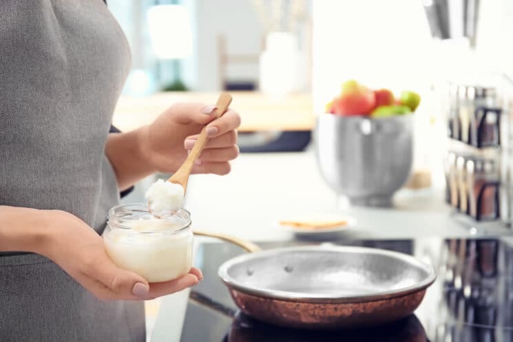 Woman at the stove about to spoon coconut oil into a pan for cooking.