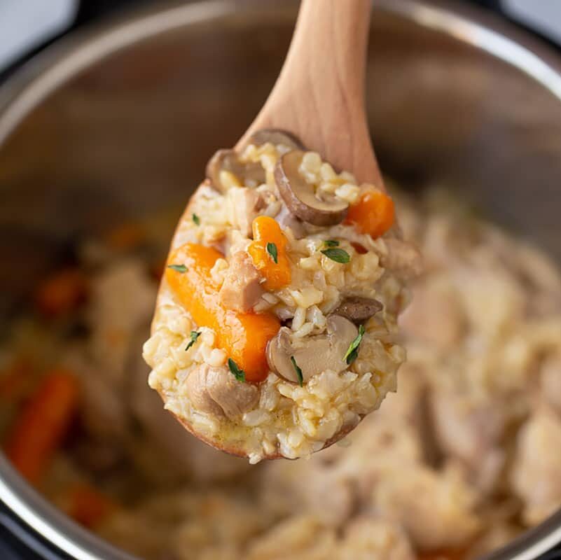 instant pot chicken and brown rice with carrots, mushrooms, on a wooden spoon over the instant pot