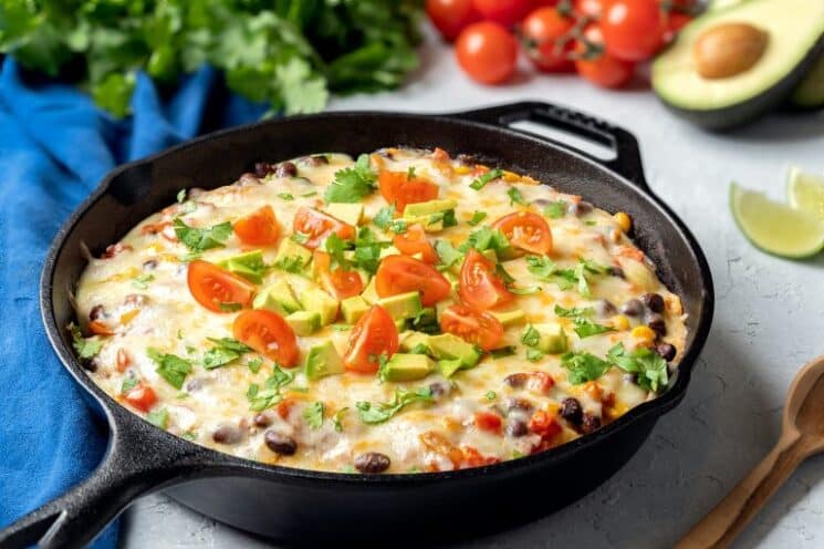 skillet with mexican enchiladas and tomatoes and avocado