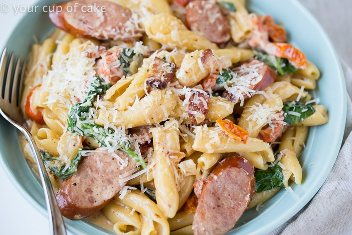 blue bowl of pasta with sausage, greens, and sundried tomatoes