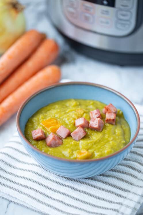 blue bowl with split pea soup and ham cubes and carrots in the background