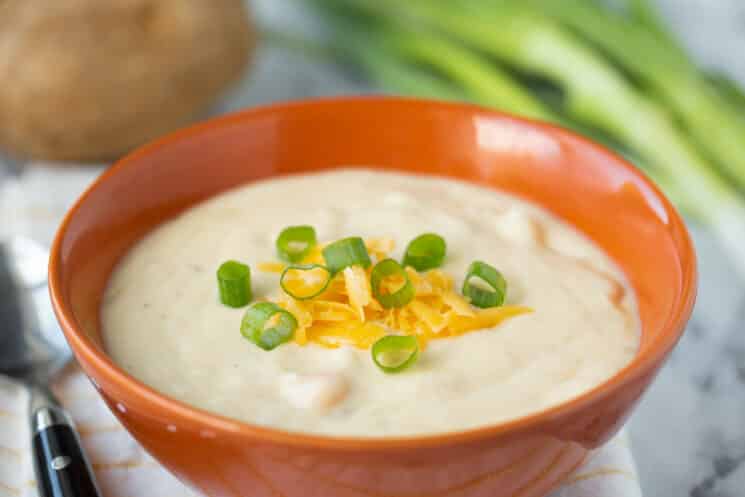 cuenco rojo con sopa de patata, queso y cebolletas