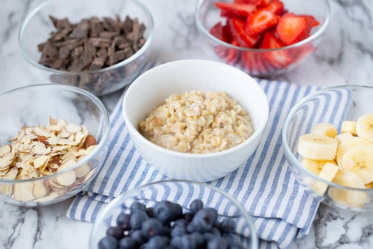 glass dishes full of many oatmeal topping ideas like strawberries, chocolate chunks, and slivered almonds