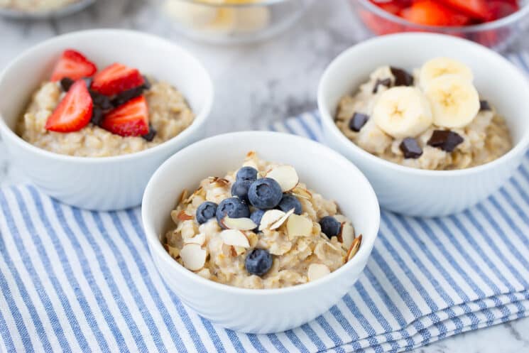 white bowls of oatmeal on a blue and white striped tablecloth are filled with an assortment of fresh toppings