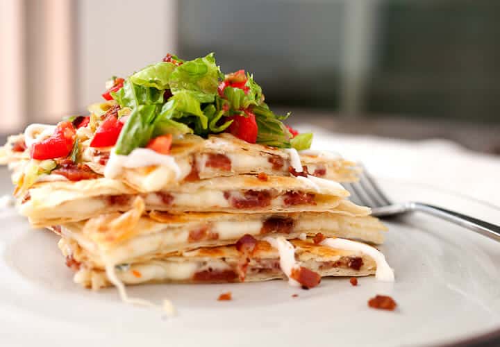 stack of cheesy quesadillas on a plate topped with lettuce and tomato