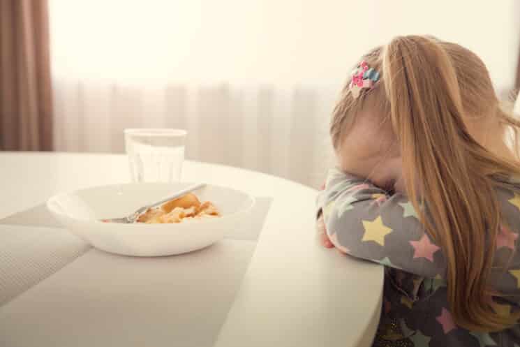 picky eater girl with her head down on the table because she doesn't want to eat