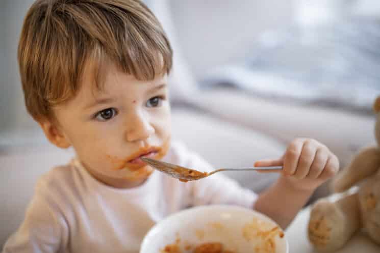 toddler boy eating from a bowl of pasta looks like he doesn't enjoy his meal