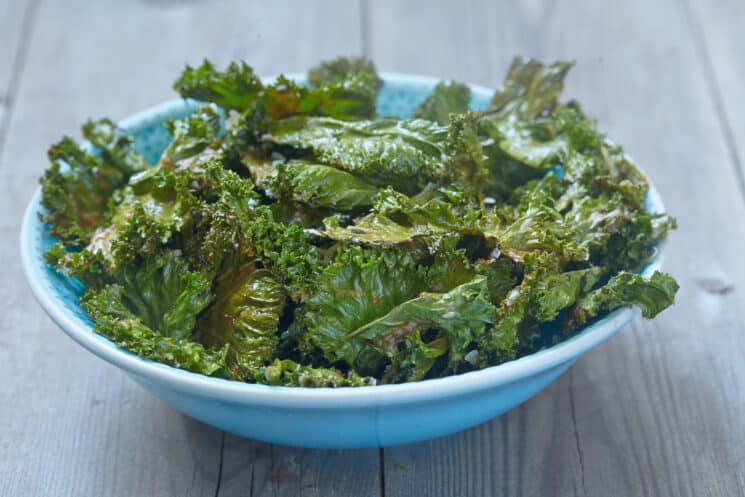 blue bowl full of kale chips on a wooden table