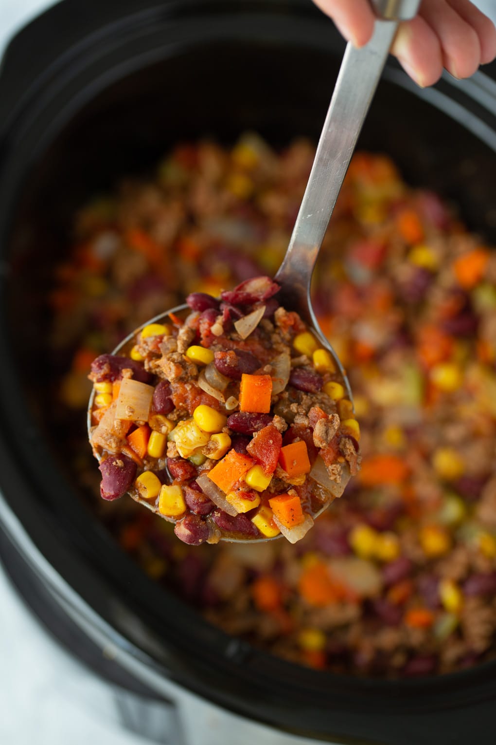 slow cooker chili with a ladle holding a scoop above the slow cooker