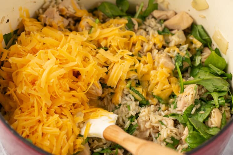 grated cheese, rice, and spinach in a pot being stirred up