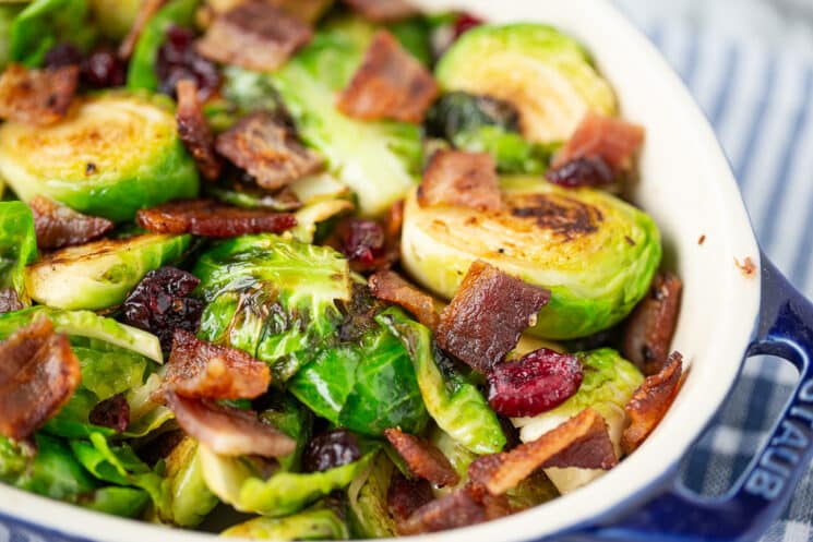 close up of cooked brussels sprouts in a dish sprinkled with crispy bacon and dried cranberries