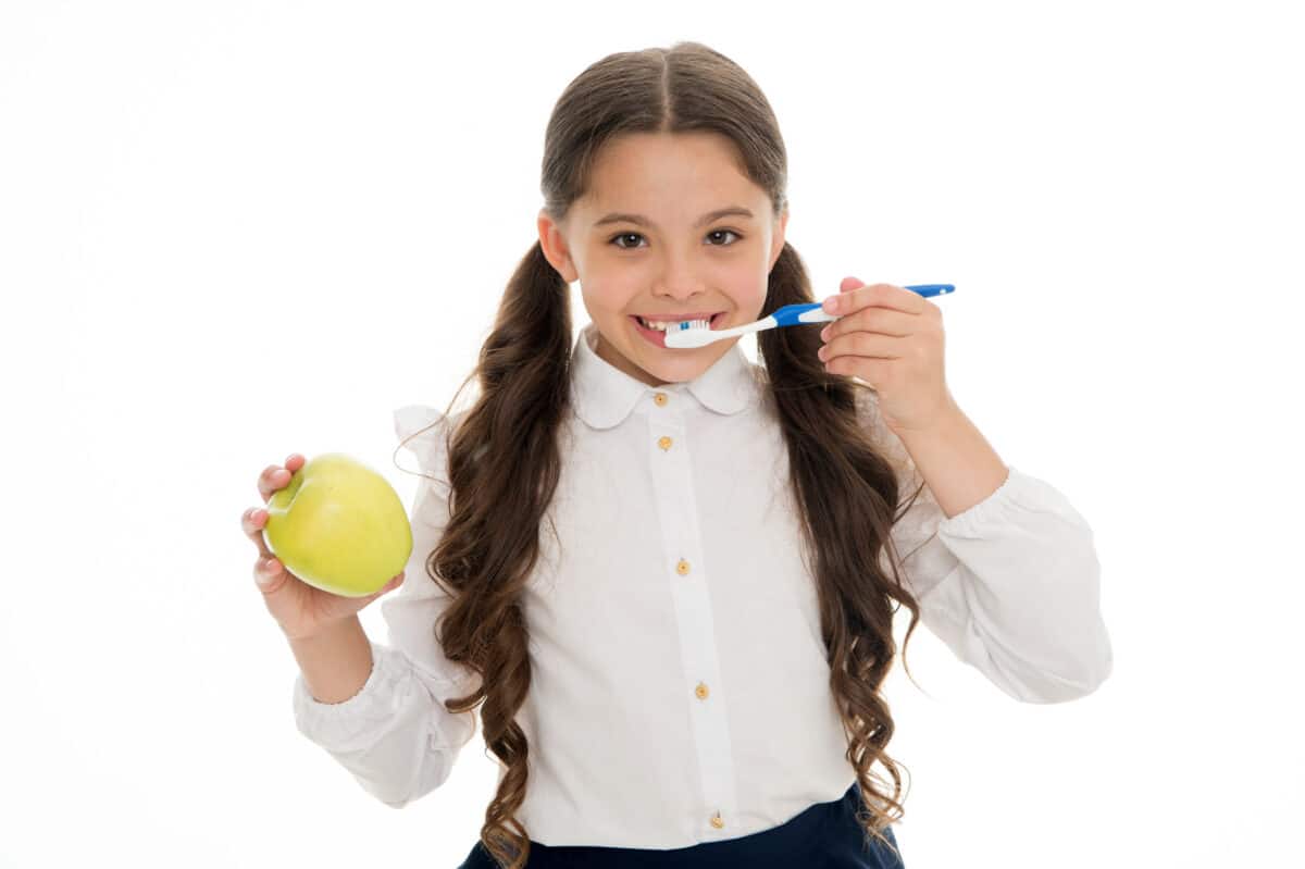 Girl holding an apple and toothbrush to show healthy habits