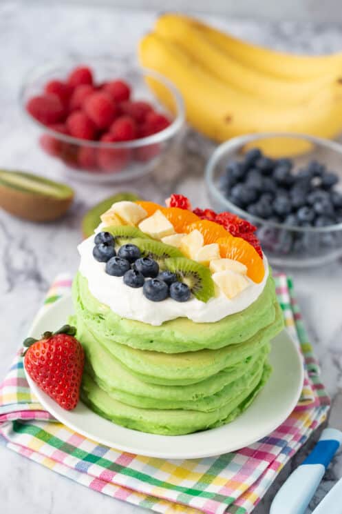 stack of spinach pancakes with whip cream and brightly colored berries on top