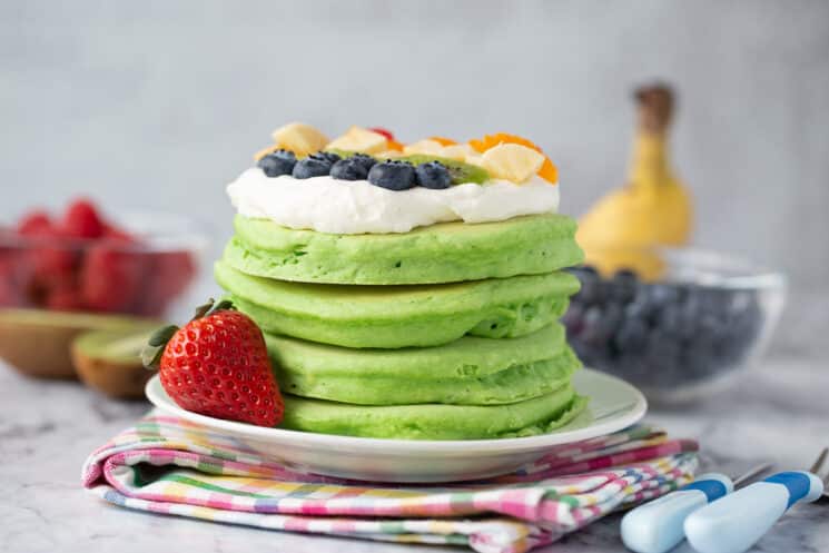 stack of spinach pancakes with whip cream and brightly colored berries on top