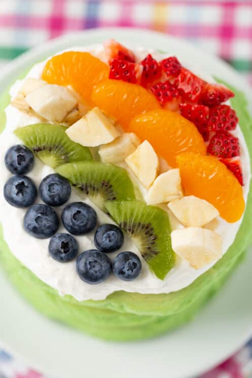 close up aerial view of stack of spinach pancakes with whip cream and brightly colored berries on top