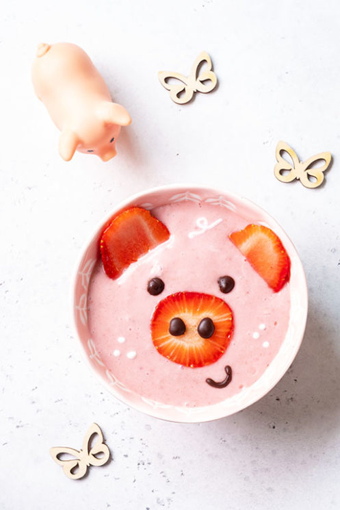 Kids strawberry smoothie bowl with a pig face made from strawberries