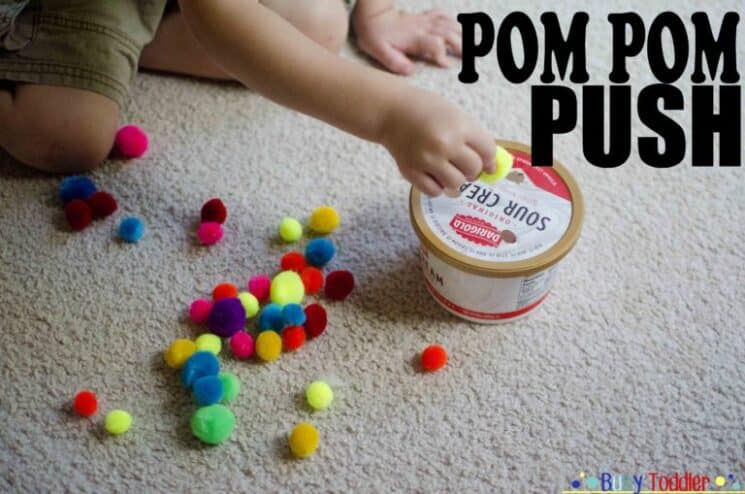 toddler pushing pom poms through the lid of a plastic container, great indoor activity for kids