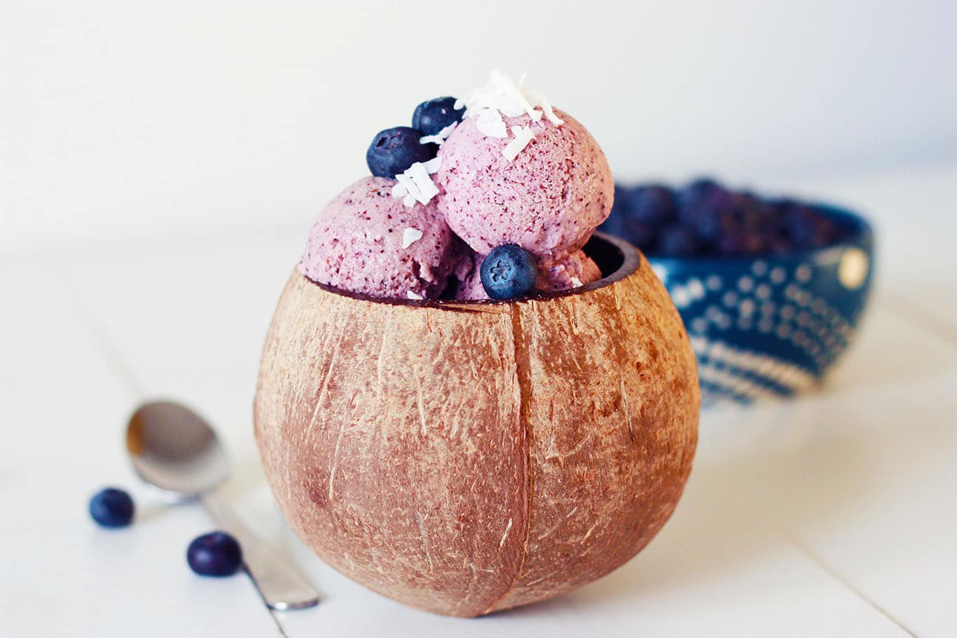 Blueberry Coconut Icecream in a coconut bowl with berries in the background