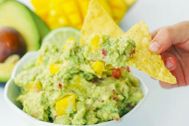 Kids hand dipping a chip in Mango Guacamole