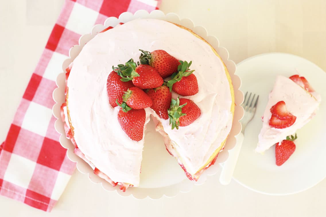 overhead view of vanilla cake with a slice taken out and strawberries on top