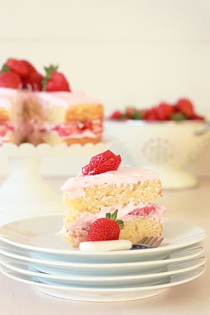 A slice of vanilla cake with strawberry frosting and strawberries on a plate