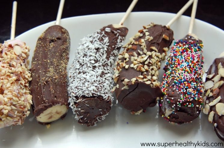 frozen bananas on sticks coated in chocolate and nuts, resting on a plate