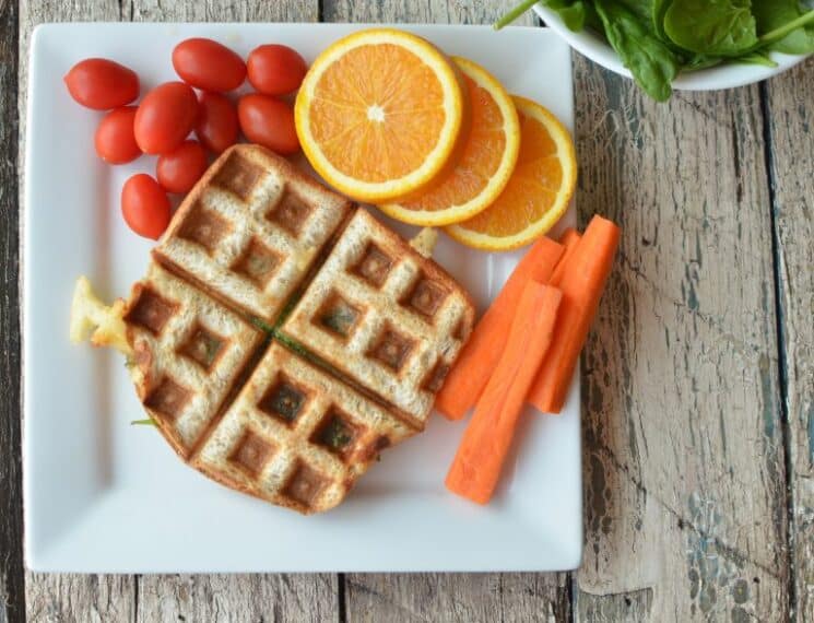 grilled cheese on a white square plate served with oranges, tomatoes and carrots