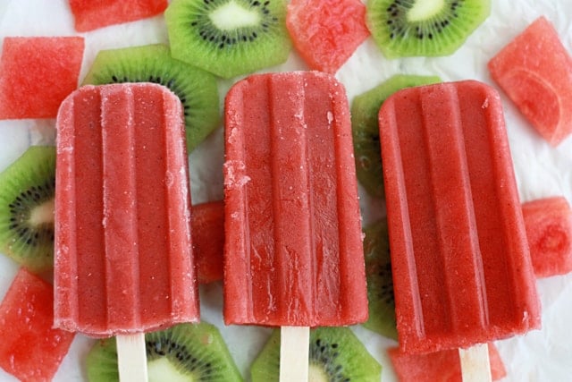 red popsicles surrounded by fresh watermelon and kiwi slices