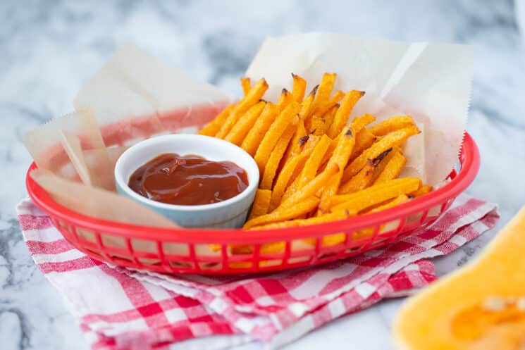 a basket of butternut squash fries with a ramekin of ketchup