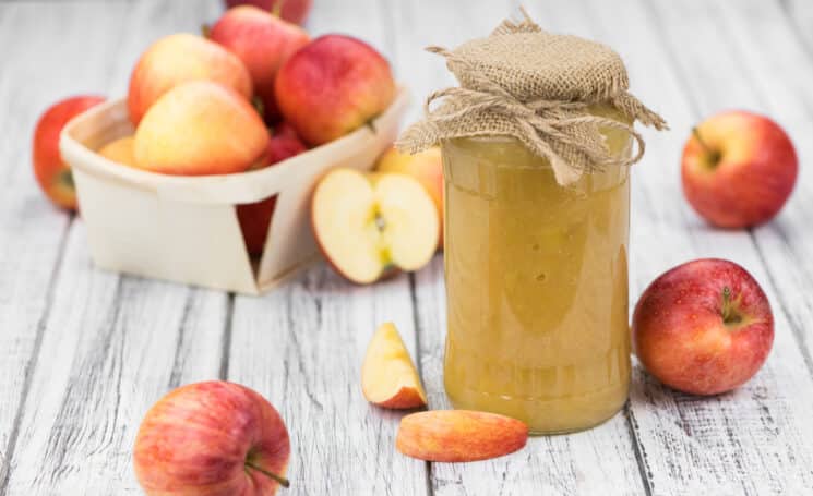 homemade applesauce in a jar with burlap around the lid.  Apples in the background