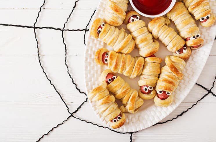 mummy hot dogs on a white plate with a black yard spider webb under the plate