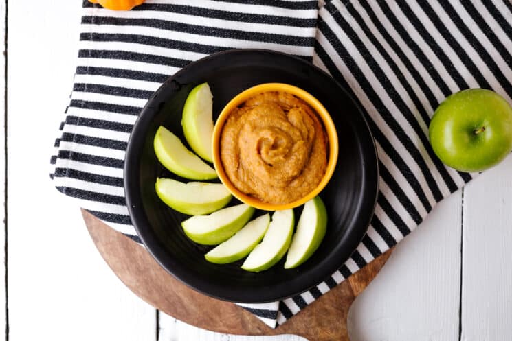 overhead view of pumpkin spice dip in a yellow bowl with green apples on a black plate