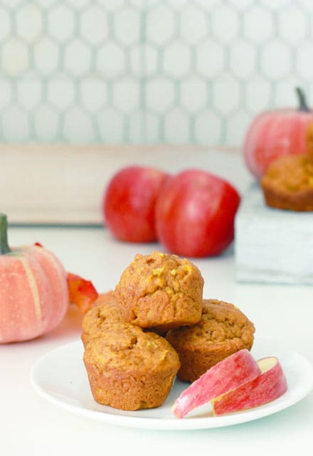 4 pumpkin apple muffins on a plate with sliced apples next to them and apples in the background