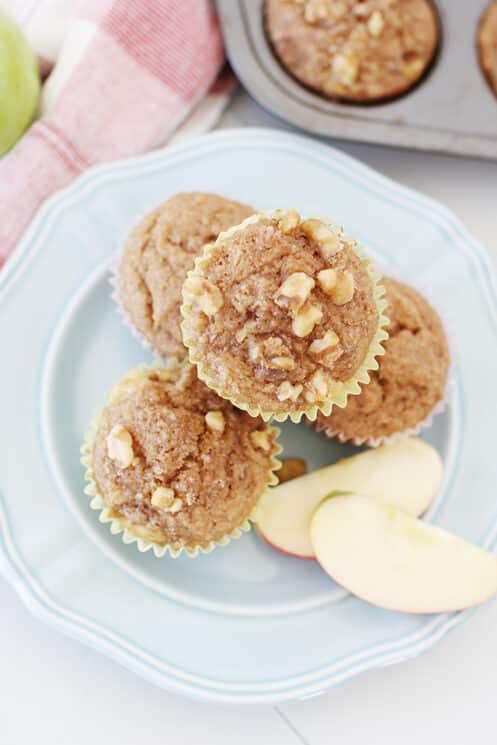 overhead view of whole wheat applesauce muffins on a plate with sliced apples