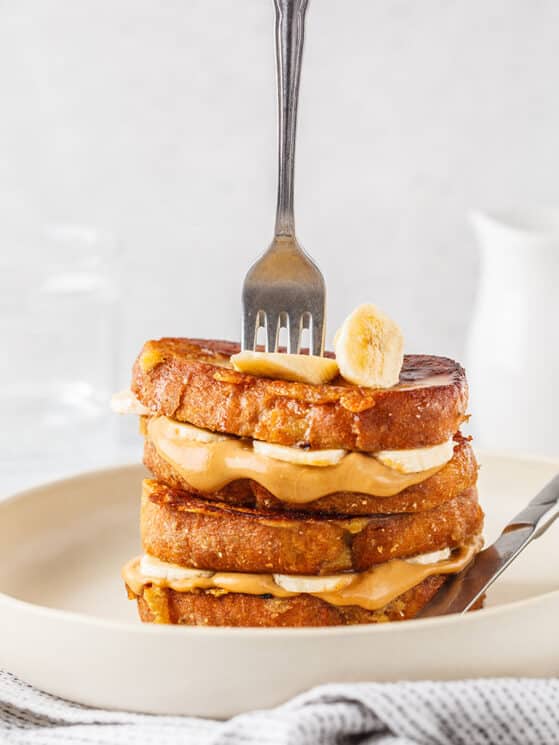 stack of peanut butter banana french toast with a fork vertically stuck in the stack