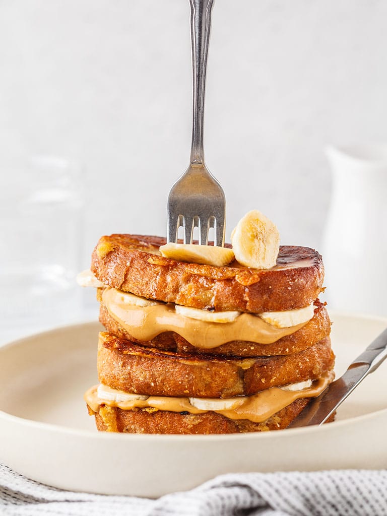 stack of peanut butter banana french toast on a plate with a fork in the stack