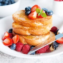 basic french toast topped with strawberries, blueberries and raspberries on a white plate