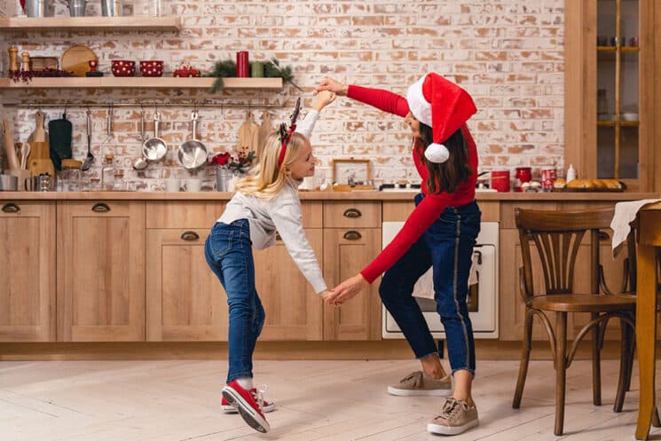 Happy child and her mother have a great time dancing in the kitchen on Christmas Eve