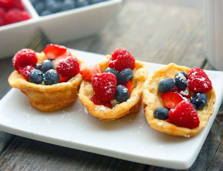 Mini puffed pancakes topped with berries and served on a white rectangular plate